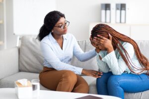 Stressed black lady suffering from depression, her counselor supporting her at medical office